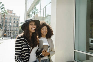 Happy female coworkers standing on street in city during sunny day - VABF03902