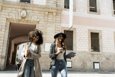 Lächelnde weibliche Mitarbeiter gehen auf der Straße vor einem Gebäude in der Stadt - VABF03904