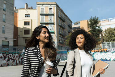 Female coworkers looking away while standing on street in city during sunny day - VABF03908