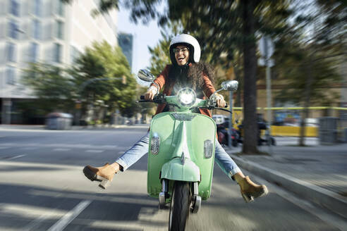Fröhliche Frau fährt Motorroller auf der Straße in der Stadt - VEGF03108