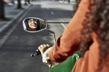 Junge Frau Reflexion auf Seite Ansicht Spiegel lachend beim Fahren Motorroller in der Stadt - VEGF03110