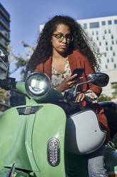 Junge Frau, die an einem sonnigen Tag in der Stadt eine SMS auf einem Smartphone schreibt - VEGF03118