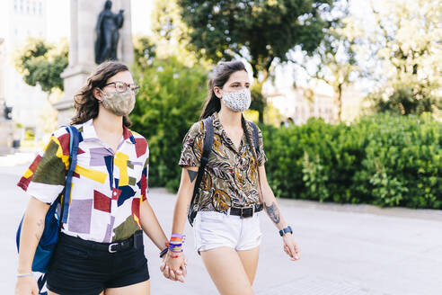 Lesbian couple wearing protective face mask walking on street in city - DGOF01593