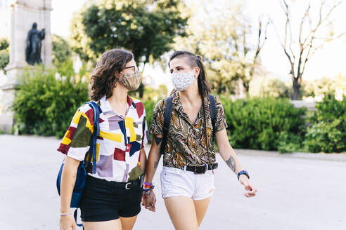 Young lesbian couple looking at each other while walking on street during COVID-19 crisis - DGOF01594