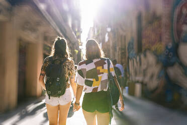 Lesbisches Paar, das an einem sonnigen Tag in einer Gasse in der Stadt spazieren geht - DGOF01595
