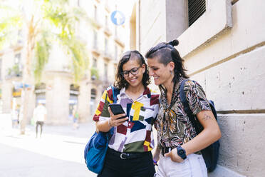 Lächelndes lesbisches Paar, das ein Smartphone benutzt, während es auf der Straße in der Stadt steht - DGOF01597