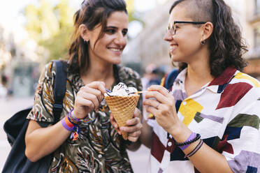 Lesbian couple holding ice cream cone while standing in city - DGOF01615