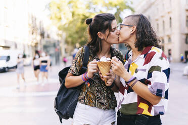 Junges lesbisches Paar hält Eis, während sie sich auf der Straße in der Stadt küssen - DGOF01616
