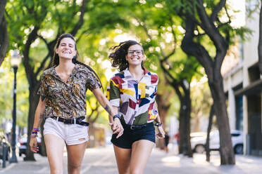 Smiling lesbian couple running on footpath in city
 - DGOF01630