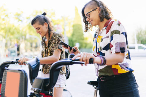 Lesbisches Paar benutzt Smartphone, um Elektrofahrrad in der Stadt zu entriegeln - DGOF01631