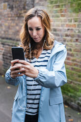 Mid adult woman photographing through mobile phone while standing in city - JMPF00526