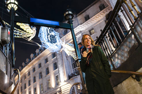 Smiling woman standing under Christmas lights on Regent Street in city at London, UK - JMPF00541