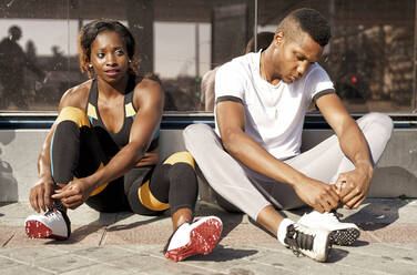 Athletes tying shoelaces while sitting on sidewalk at city - GGGF00061