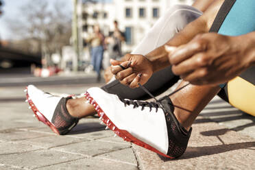 Sportswoman typing shoelace while sitting by man on sidewalk at city - GGGF00062