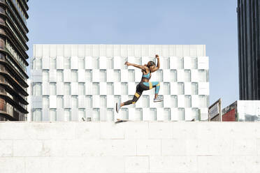 Young female athlete running on wall in city - GGGF00065