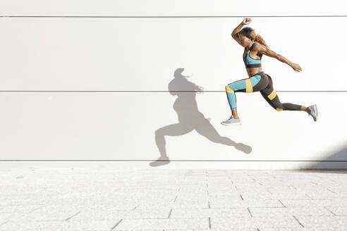 Young woman running against white wall at city - GGGF00068