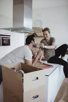 Lächelnde Frau füttert männlichen Partner mit Pizza, während sie in neuem Haus auf dem Küchentisch sitzt - MASF20377