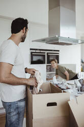 Mann schaut eine Frau an, während er im neuen Haus Pappkartons auspackt - MASF20382