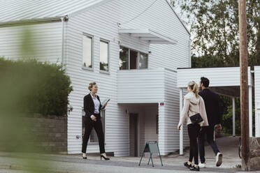 Smiling real estate professional talking to couple outside new house - MASF20404
