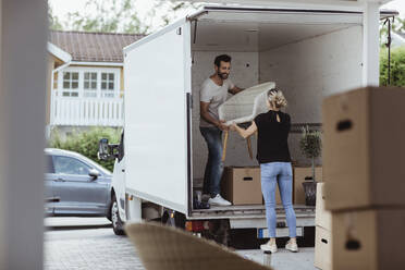 Smiling male and female partners unloading chair from van - MASF20420