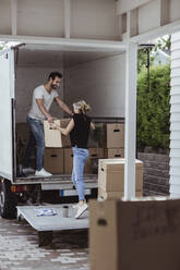 Smiling male and female partners unloading luggage during relocation - MASF20423