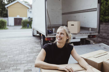 Lächelnde Frau an Pappkarton, die vor dem Lieferwagen wegschaut - MASF20430