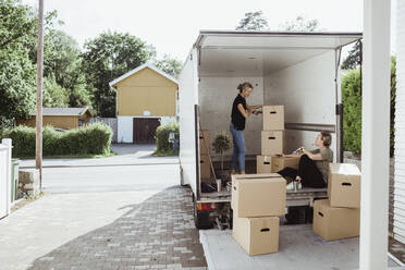 Side view of woman with boxes talking to female friend in moving van - MASF20436