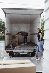 Seitenansicht einer Frau, die eine müde Frau an einem Pappkarton im Lieferwagen anschaut - MASF20437