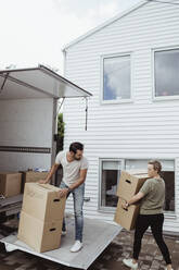 Male and female partners unloading cardboard boxes during relocation - MASF20442