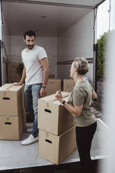 Male and female friends talking while unloading cardboard boxes during relocation - MASF20444