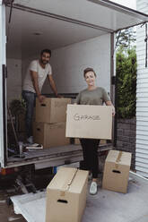 Porträt von lächelnden männlichen und weiblichen Partnern beim Entladen von Pappkartons aus einem Lieferwagen - MASF20447
