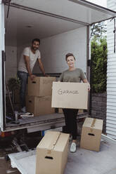 Portrait of smiling male and female partners unloading cardboard boxes from van - MASF20447