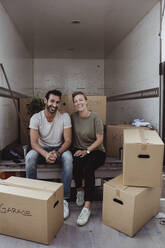 Portrait of smiling male and female partners sitting by cardboard boxes in van - MASF20448