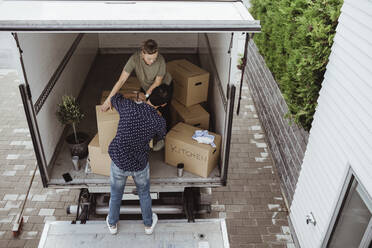 Rear view of male helping female carrying cardboard boxes outside van - MASF20454