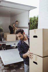 Male helping female friend unloading cardboard boxes outside van - MASF20455