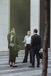 Smiling female entrepreneur talking to colleagues while standing in city - MASF20472