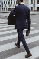 Rear view of male entrepreneur with bag and file crossing road n city - MASF20482