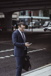 Businessman with bag using smart phone while standing in city - MASF20488