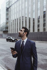 Male entrepreneur using smart phone while looking up in city - MASF20498