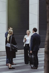 Smiling female entrepreneur talking to coworkers while standing in city - MASF20508