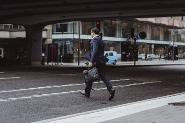 Businessman with bag crossing road in city - MASF20518