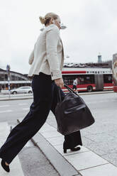 Side view of entrepreneur with bag walking in city - MASF20521