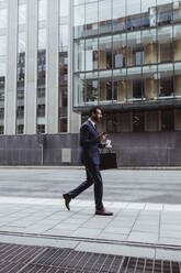 Unternehmer mit Tasche, der beim Spaziergang in der Stadt ein Smartphone benutzt - MASF20533