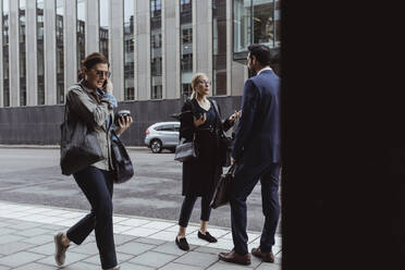 Female entrepreneur with bag talking to male coworker in city - MASF20534