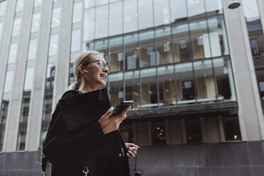 Low angle view of businesswoman talking through in-ear headphones in city - MASF20540