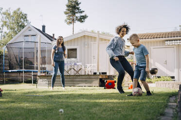 Mother and son playing soccer while woman standing in backyard - MASF20565