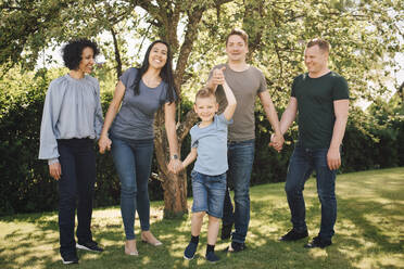 Portrait of playful son holding hands with smiling homosexual parents in backyard - MASF20573