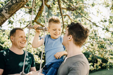 Homosexuelle Väter sehen lächelnden Sohn beim Spielen im Garten - MASF20586