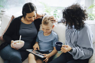 Sohn benutzt digitales Tablett auf dem Sofa von lesbischen Müttern zu Hause - MASF20589