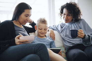 Lächelnder Sohn mit digitalem Tablett auf dem Sofa von lesbischen Müttern zu Hause - MASF20590